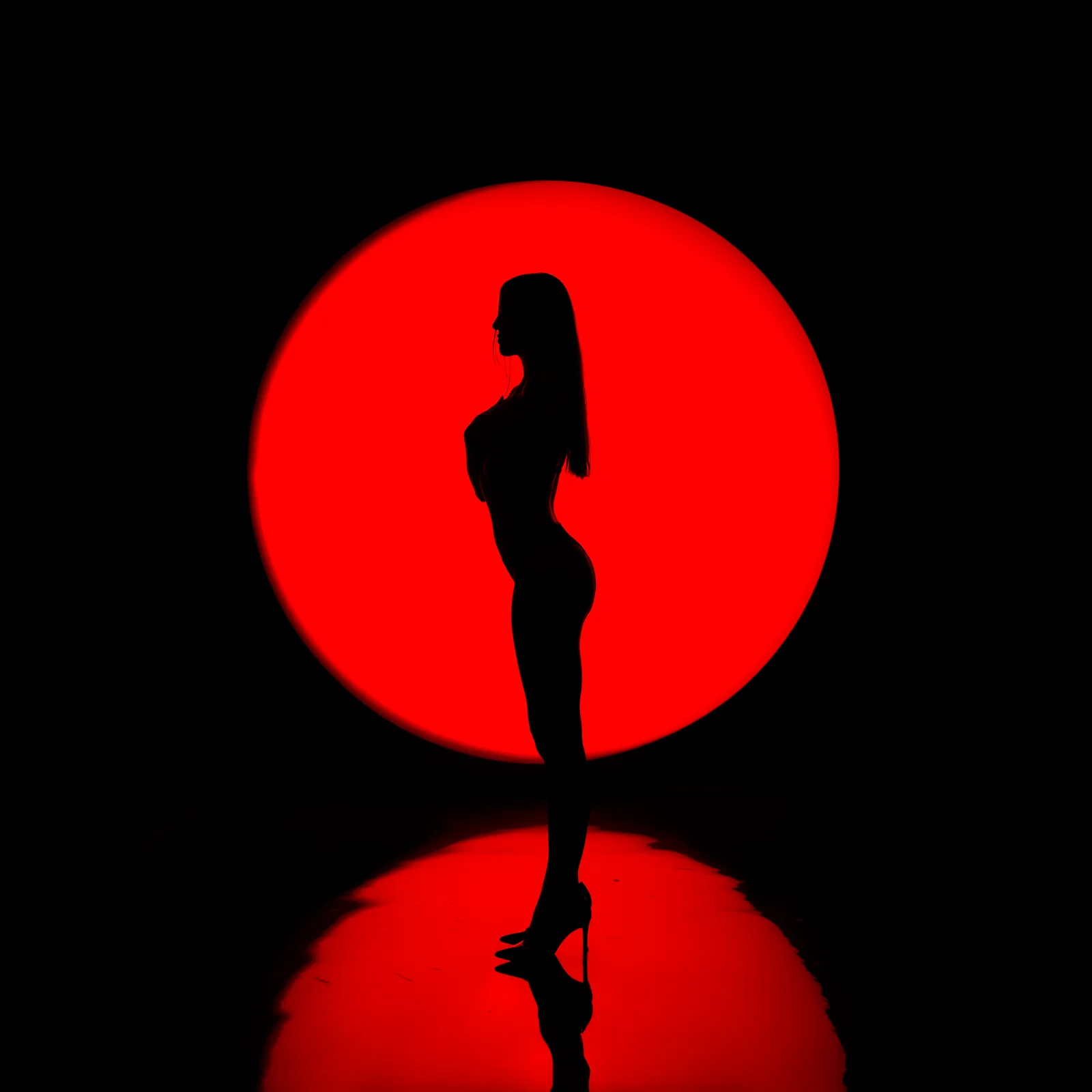 Silueta femenina de pie contra un círculo de luz roja con reflejo en el suelo
